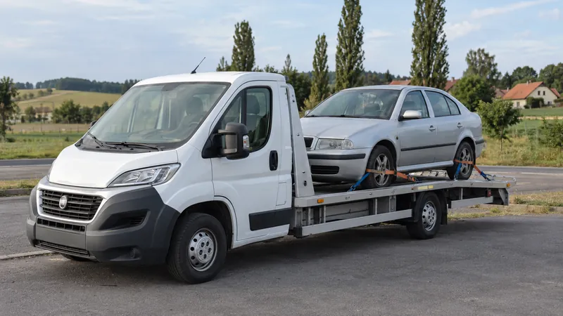 Lehký bílý odtahový vůz s upevněným automobilem Škoda